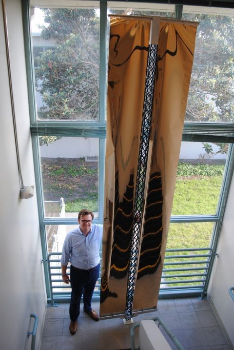 Made in Space CEO Andrew Rush pictured next to a subscale version of a solar array that the company can produce in space. The golden Mylar pieces are physical mockups of what would be solar blankets. This solar array is over 3 m tall. (Made in Space)